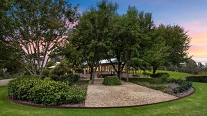 Un jardín arbolado con una casa, rodeado de árboles y céspedes cuidados.