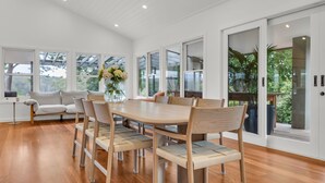 Un comedor con mesa y sillas de madera, un sofá y ventanas amplias con vista a la vegetación.