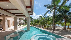 A swimming pool with a hot tub, surrounded by palm trees and lounge chairs, with a view of the ocean.