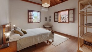 Ein Schlafzimmer mit einem hölzernen Bett, Nachttischlampen, einem Holzschrank und einem Fenster mit Blick ins Freie.