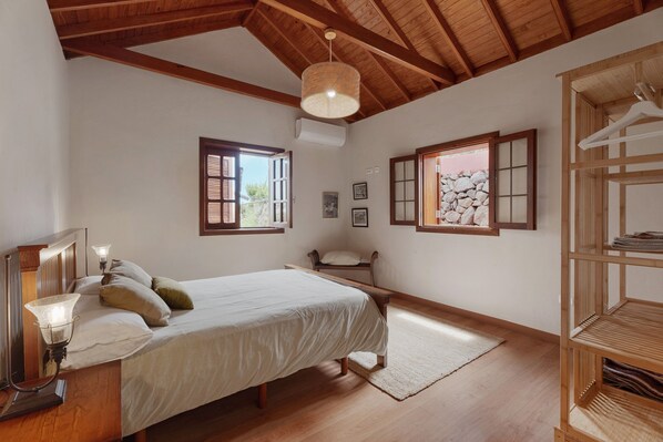 A bedroom with a wooden bed, bedside lamps, a wooden wardrobe, and a window with a view of the outside.