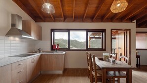 Eine Küche mit Holzausstattung, einer Edelstahl-Dunstabzugshaube, einem großen Fenster und einem Essbereich mit Holztisch und Stühlen.