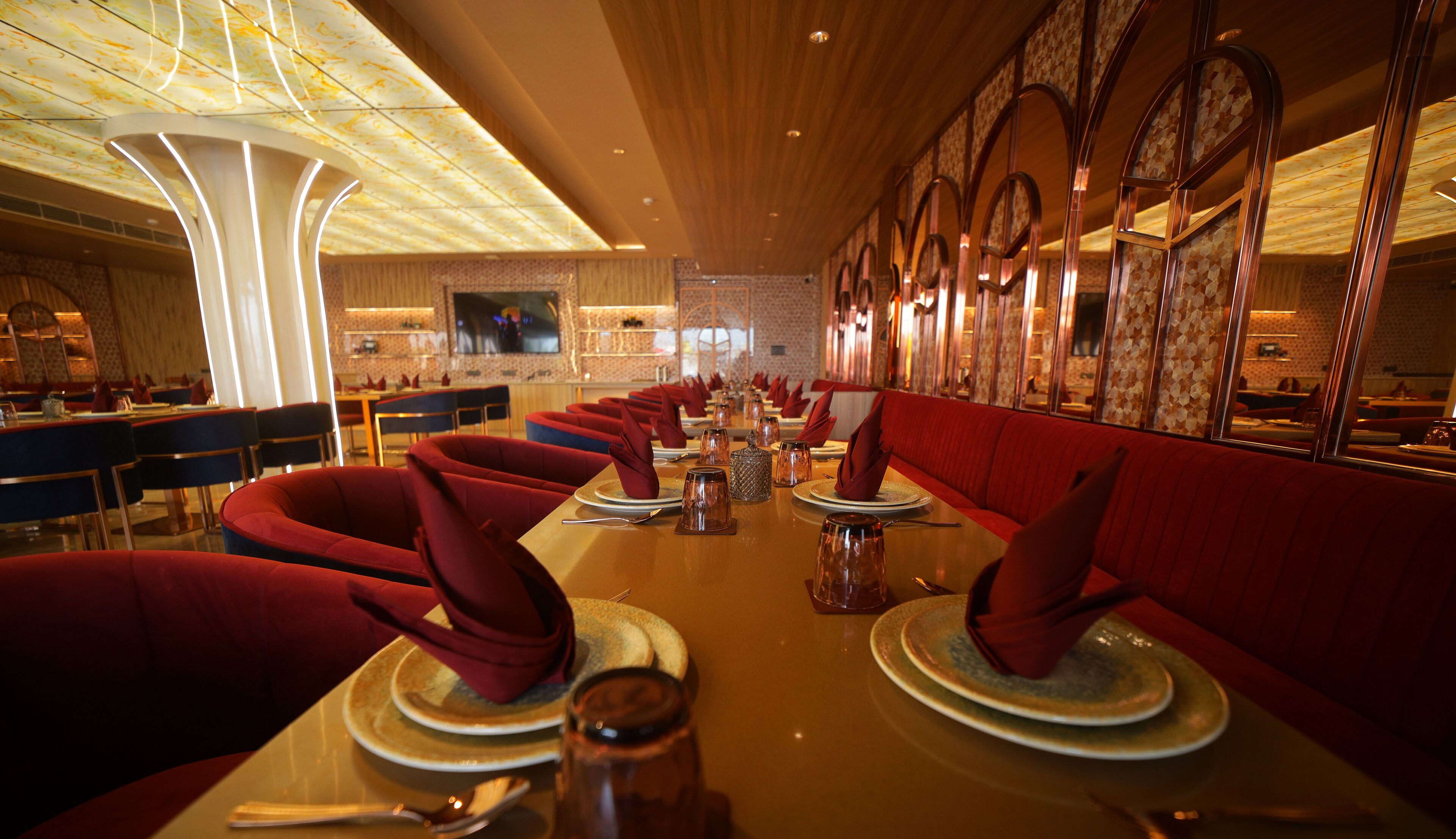 A restaurant with red upholstered booths, a long communal table, and a patterned ceiling.