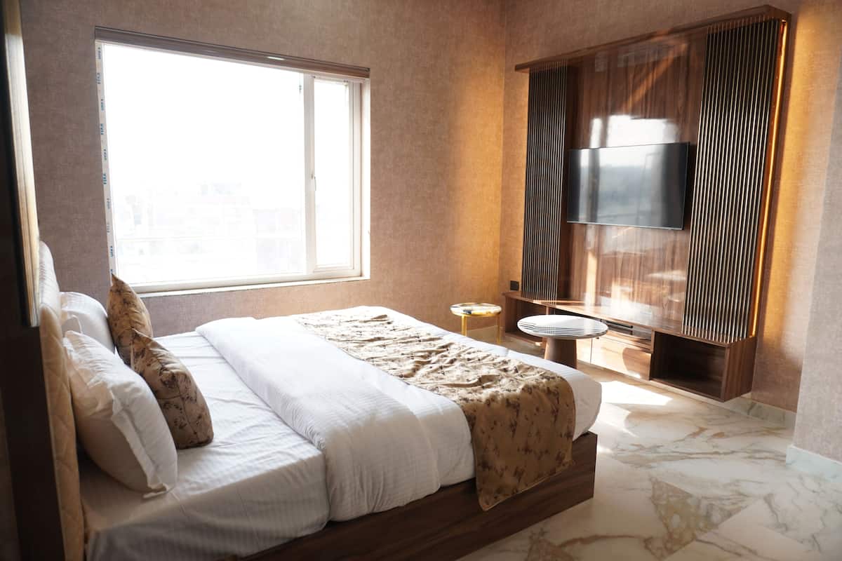 Ein modernes Hotelzimmer mit einem großen Bett, einem an der Wand montierten Fernseher, einem kleinen Tisch und einem Fenster, das natürliches Licht hereinlässt.