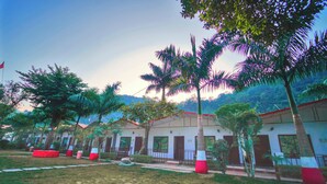 A row of white buildings with red trim, surrounded by palm trees and greenery. - Antaram Resort (Rishikesh)