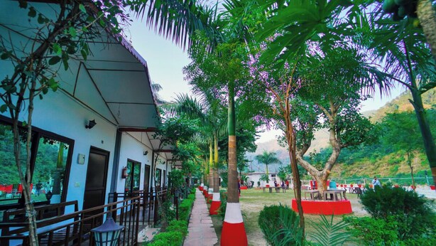 A pathway lined with trees and benches, leading to a building with a blue exterior and a covered outdoor seating area. - Antaram Resort (Rishikesh)