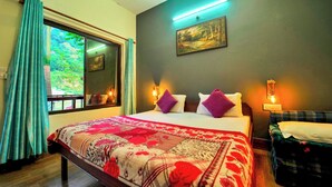 A bedroom with a large bed, a window with curtains, a painting on the wall, and a bedside table with a lamp. - Antaram Resort (Rishikesh)