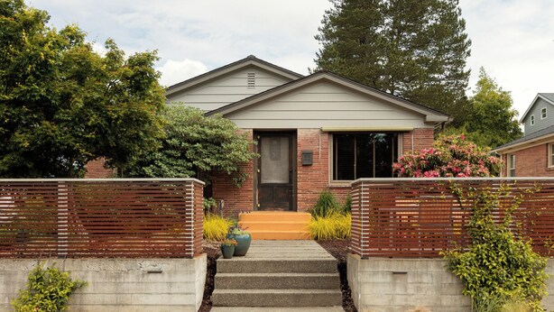 A two-story house with a front porch, a brick exterior, and a small garden with various plants and flowers.