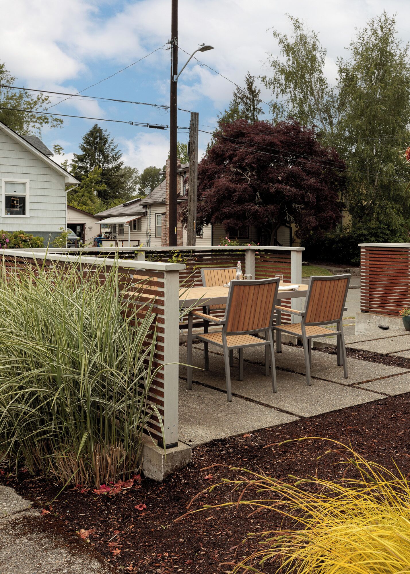 An outdoor patio area with a table and chairs, surrounded by a wooden fence and various plants.