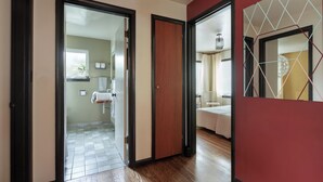 A hallway with wooden flooring, a mirror, and a door leading to a bathroom with a toilet and sink.