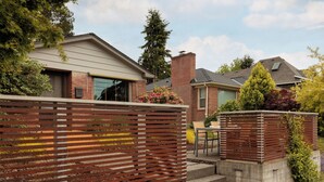 A residential area with a modern house featuring a brick exterior, a large window, and a small garden with a wooden fence.