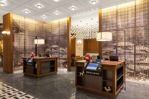 A hotel reception area with wooden reception desks, a digital display, and a decorative wall with a grid pattern. - UrCove by Hyatt Xi'an Bell Tower Huimin Street (Xi'an)