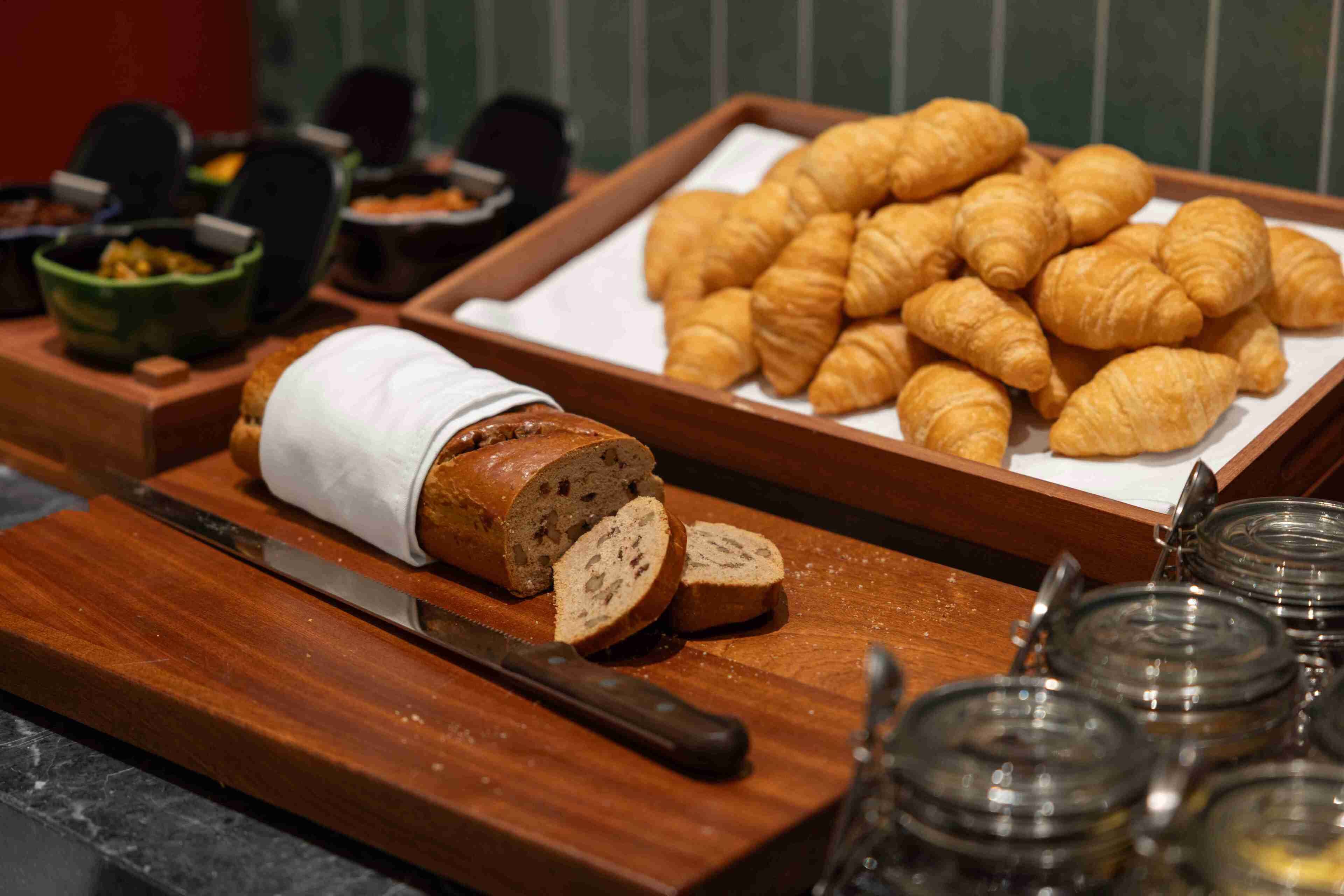Un buffet de petit-déjeuner comprenant des croissants, du pain tranché et diverses garnitures.
