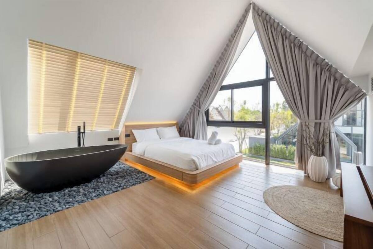 A modern bedroom with a large bed, a black bathtub, and a view of the outdoors.