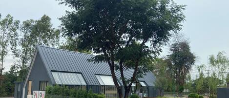 Un edificio moderno con techo inclinado, ventanas amplias y un área pavimentada con valla.