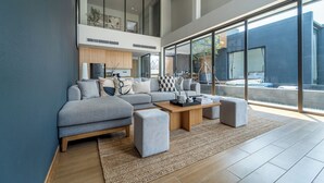 Ein modernes Wohnzimmer mit einer grauen Sofagarnitur, einem Holztisch und einem großen Fenster mit Blick ins Freie.