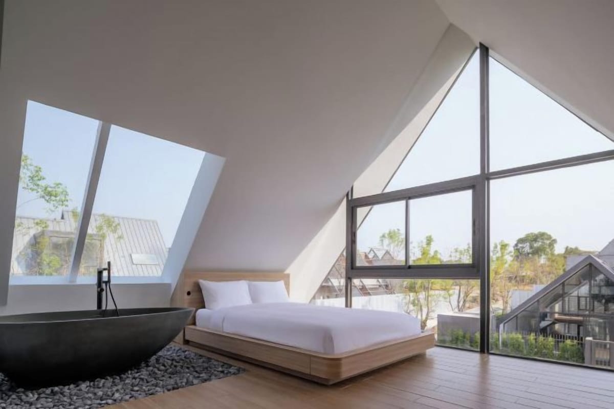 A modern bedroom with a large bed, a black bathtub, and large windows offering a view of the outside.