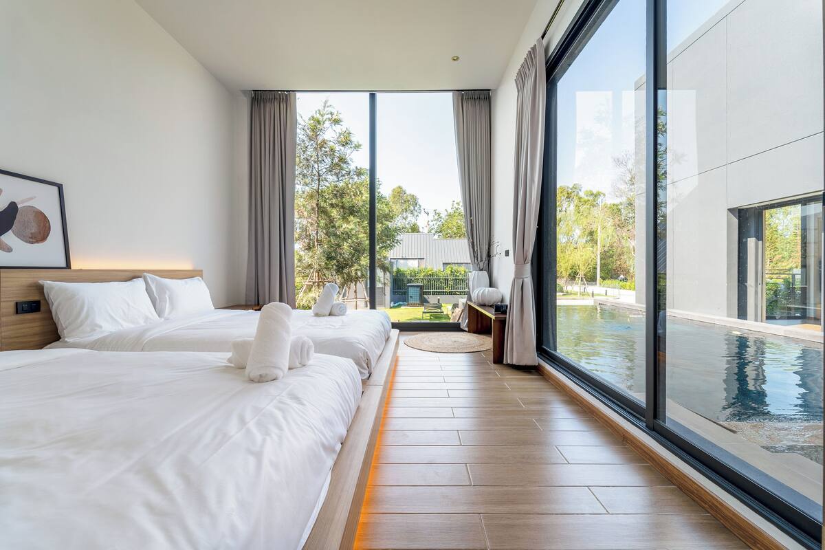 A modern hotel room with two beds, a large window, and a view of a swimming pool.
