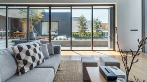 Ein modernes Wohnzimmer mit einem grauen Sofa, einem Couchtisch und Blick durch große Fenster nach draußen.
