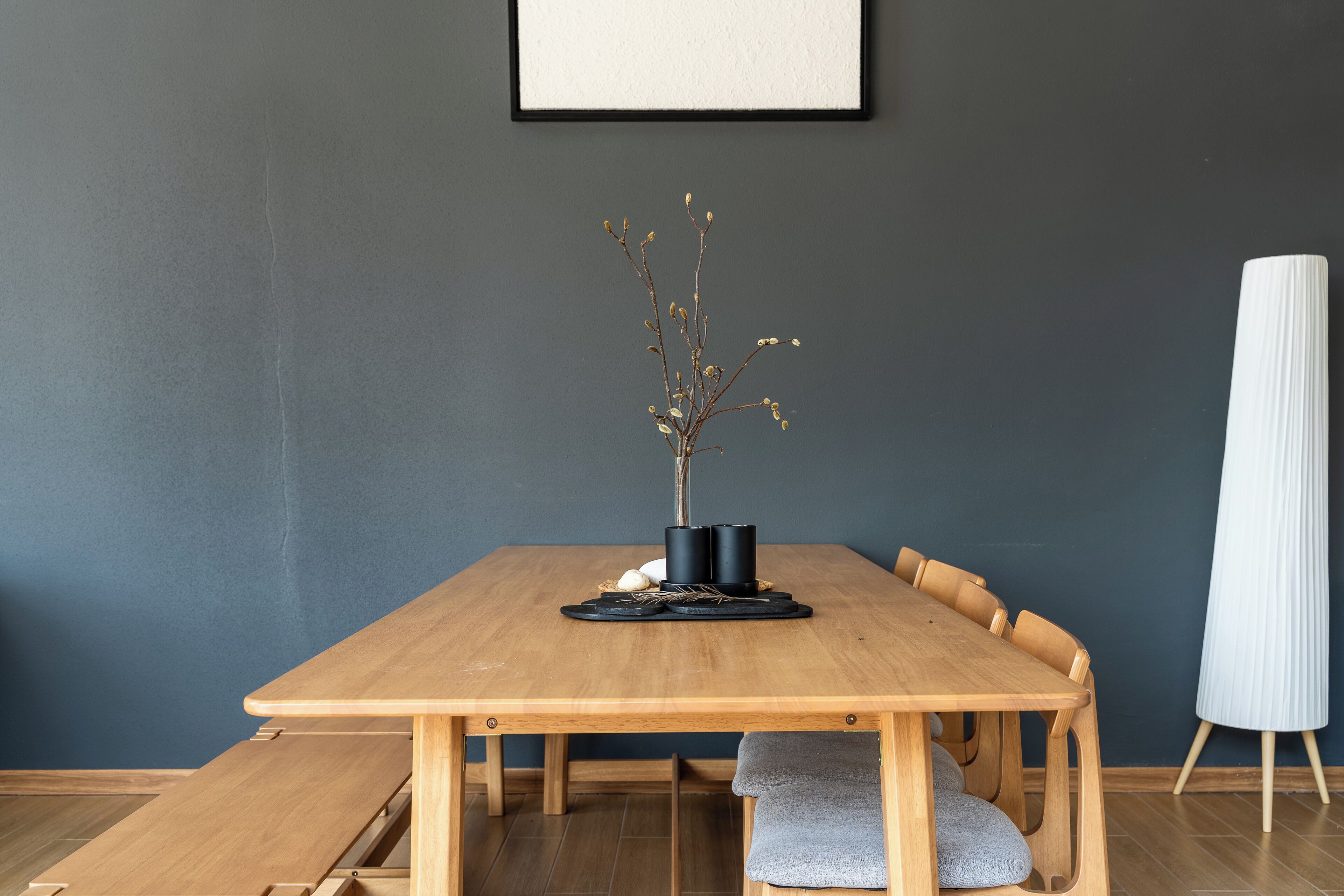 A wooden dining table with chairs, a vase with branches, and a white stand.
