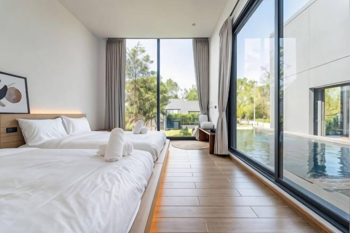 A modern hotel room with two beds, a large window with a view of a swimming pool, and a balcony.