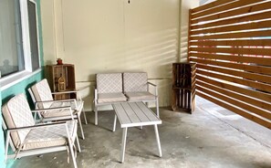 Un petit espace extérieur aménagé, à l’abri, avec un canapé, deux fauteuils et une table.