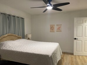 Une chambre à coucher avec un lit, un ventilateur de plafond, une table de chevet avec une lampe et deux tableaux encadrés au mur.