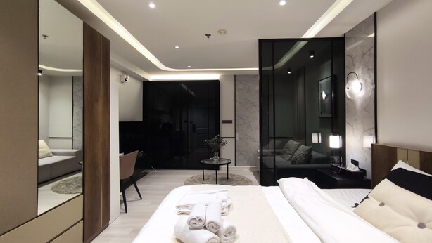 Habitació d'hotel moderna amb un llit gran, una zona d'estar amb un sofà i cadires, una taula petita i un mirall gran.