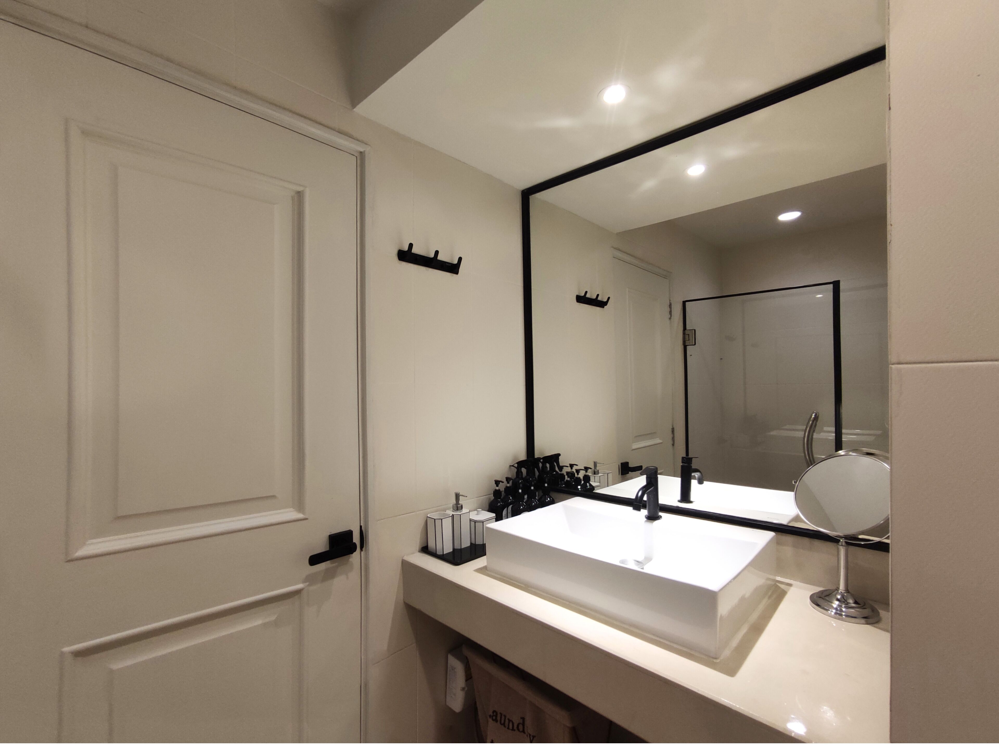 A modern bathroom with a large mirror, white sink, and black towel rack.
