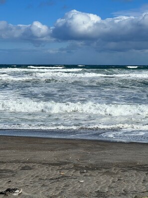 Une plage avec des vagues, un ciel dégagé et des nuages.
