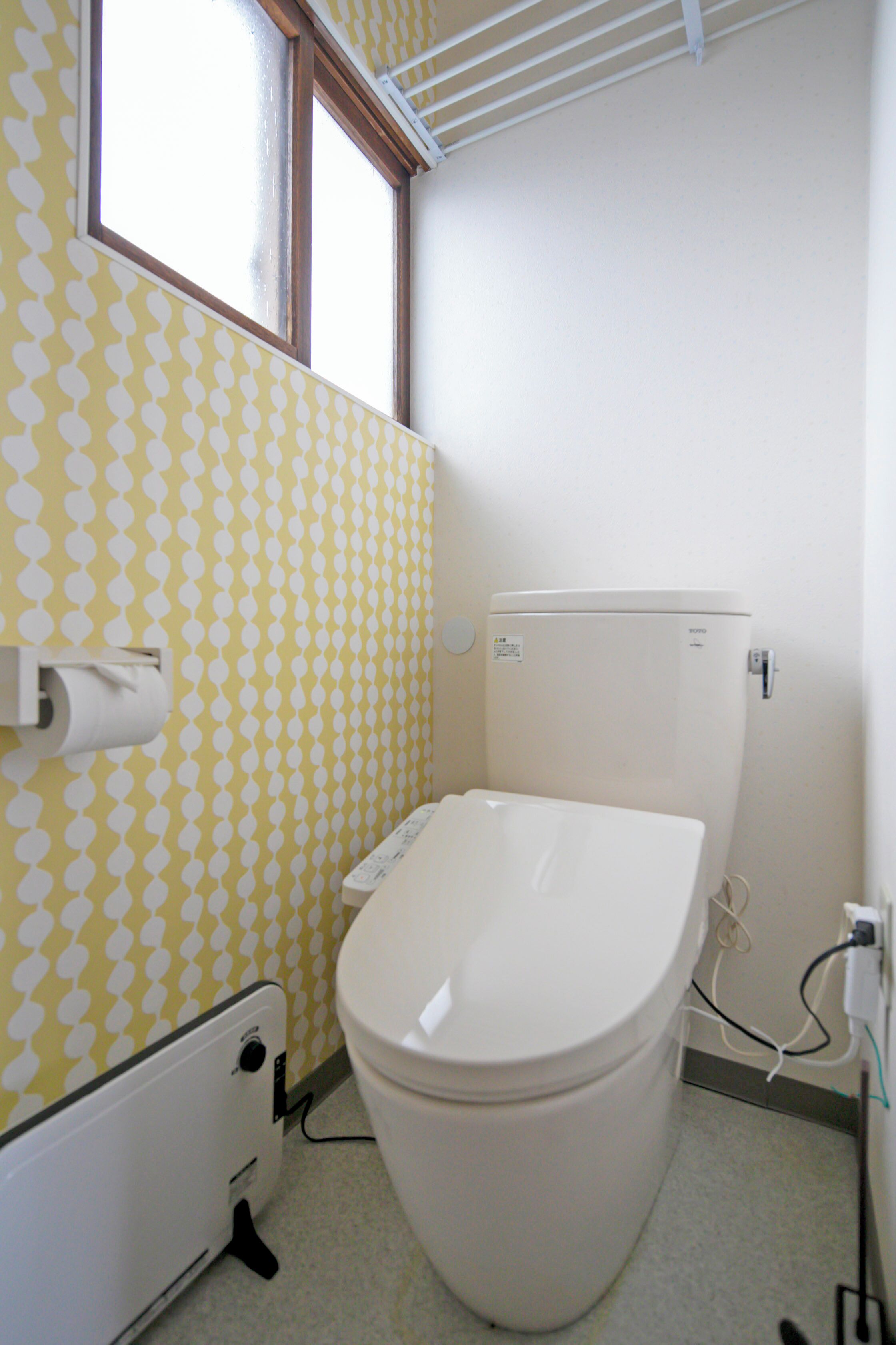 A small bathroom with a toilet, a roll of toilet paper, a radiator, and a window.