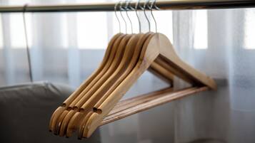 A wooden hanger on a metal rod in a room with a grey couch and a window with sheer curtains.
