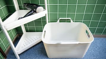 Een witte plastic plank met een haardroger en een witte plastic mand op een blauw tapijt.