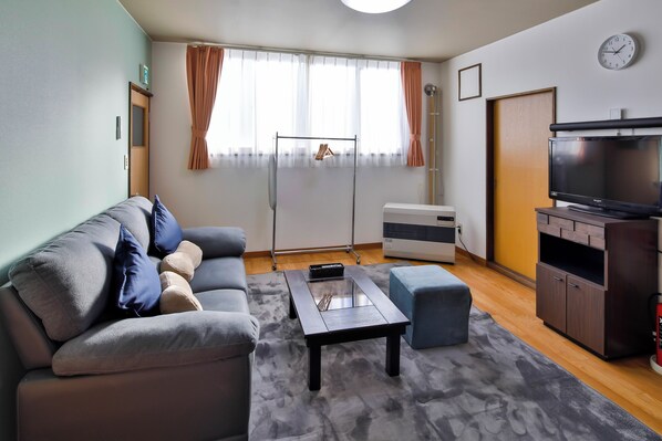 Una sala de estar con sofá, mesa de centro, televisor y ventana con cortinas.