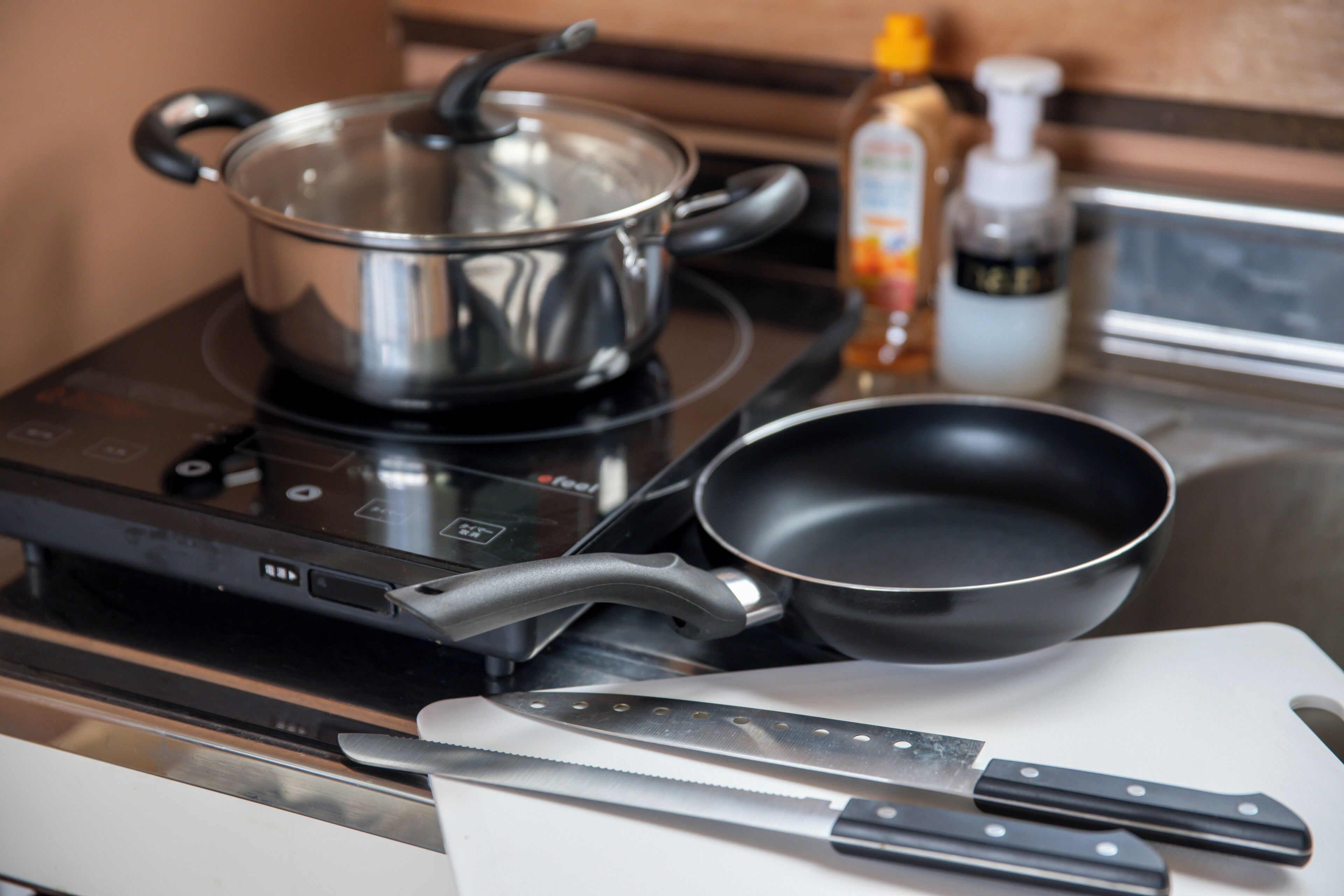 Una cocina con estufa, sartén, olla y cuchillo sobre tabla de cortar.