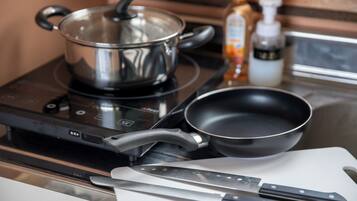 Una cocina con estufa, sartén, olla y cuchillo sobre tabla de cortar.