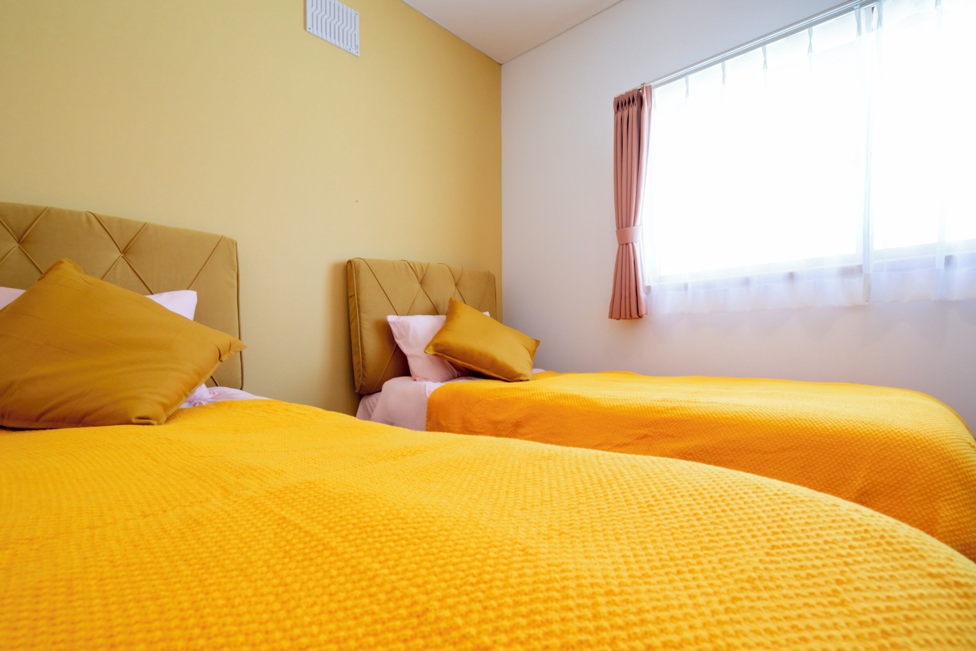 A hotel room with two beds, each with a headboard and a yellow bedspread.
