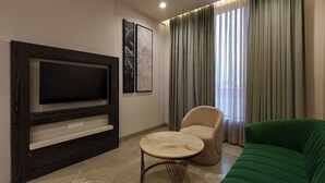 A modern living room with a flat-screen TV, a round coffee table, a beige armchair, and a green sofa. - Elinor Hotel (Agra)