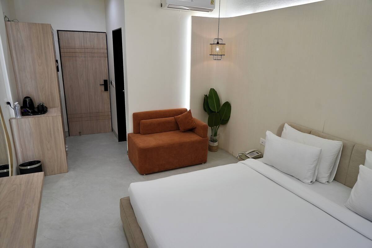 Una habitación de hotel moderna con una cama, un sillón marrón, una planta en maceta y un armario.