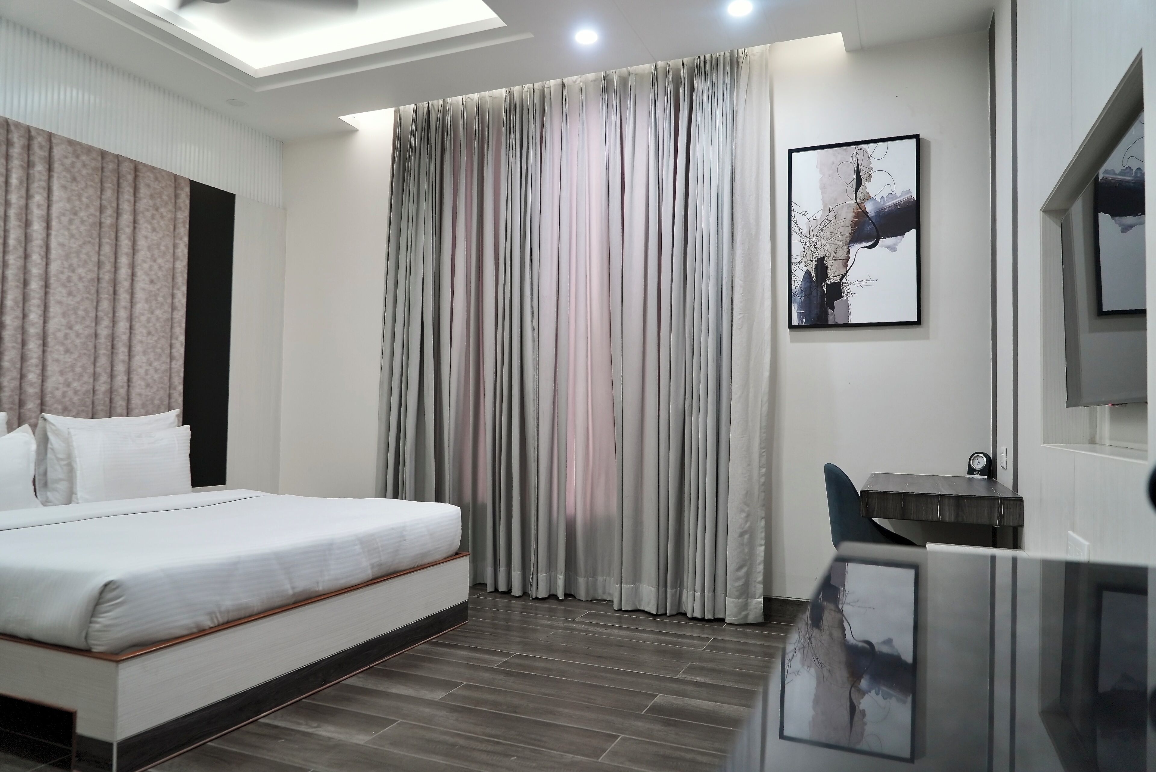 Habitación de hotel moderna con una cama grande, un escritorio y un amplio ventanal con cortinas.