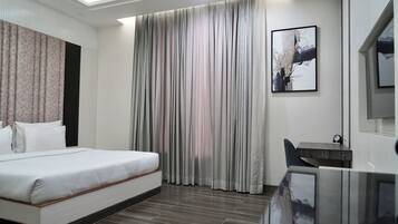 Habitación de hotel moderna con una cama grande, un escritorio y un amplio ventanal con cortinas.