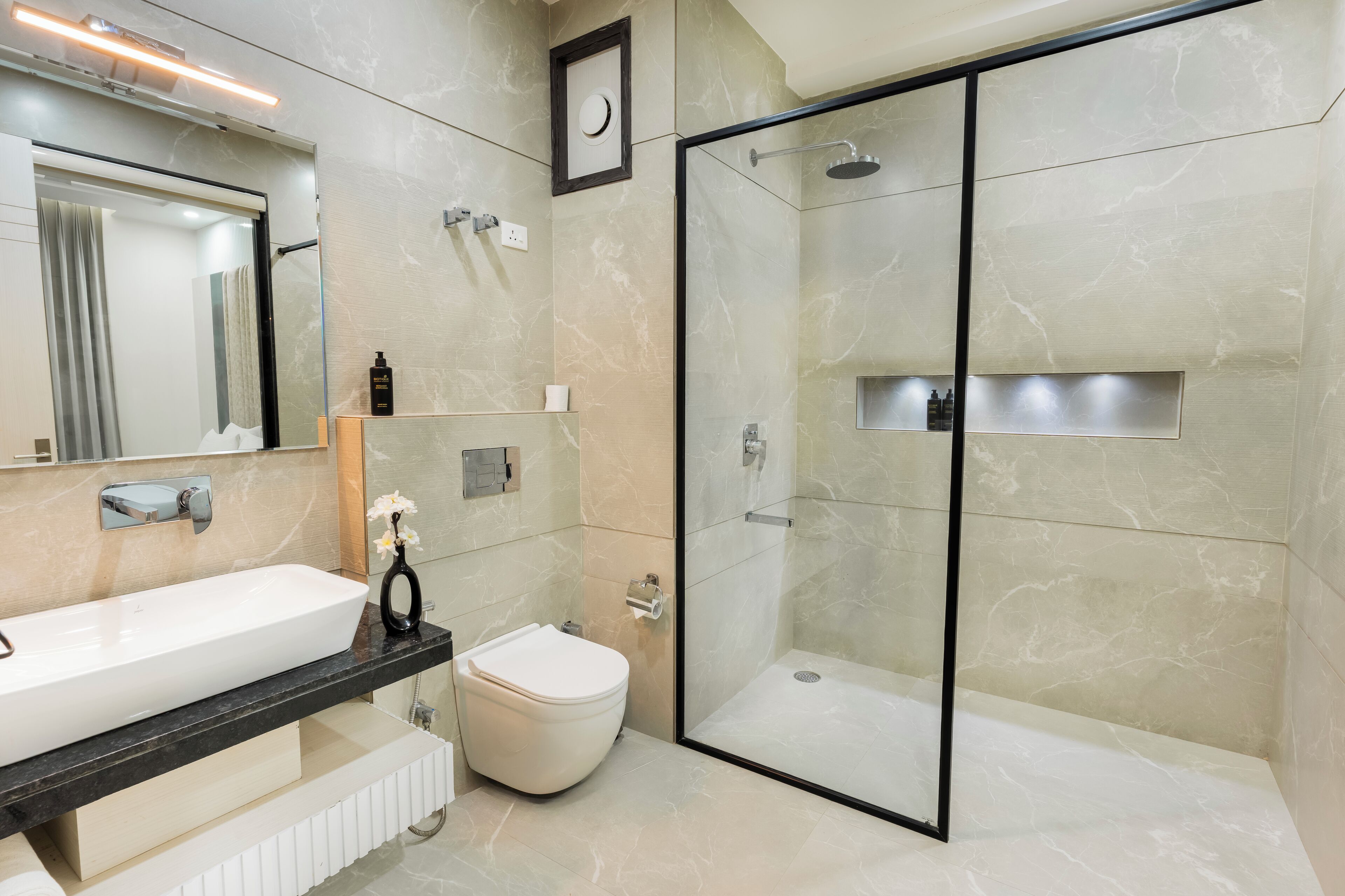 A modern bathroom with a large mirror, a white sink, a toilet, and a glass-enclosed shower area.