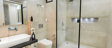A modern bathroom with a large mirror, a white sink, a toilet, and a glass-enclosed shower area.