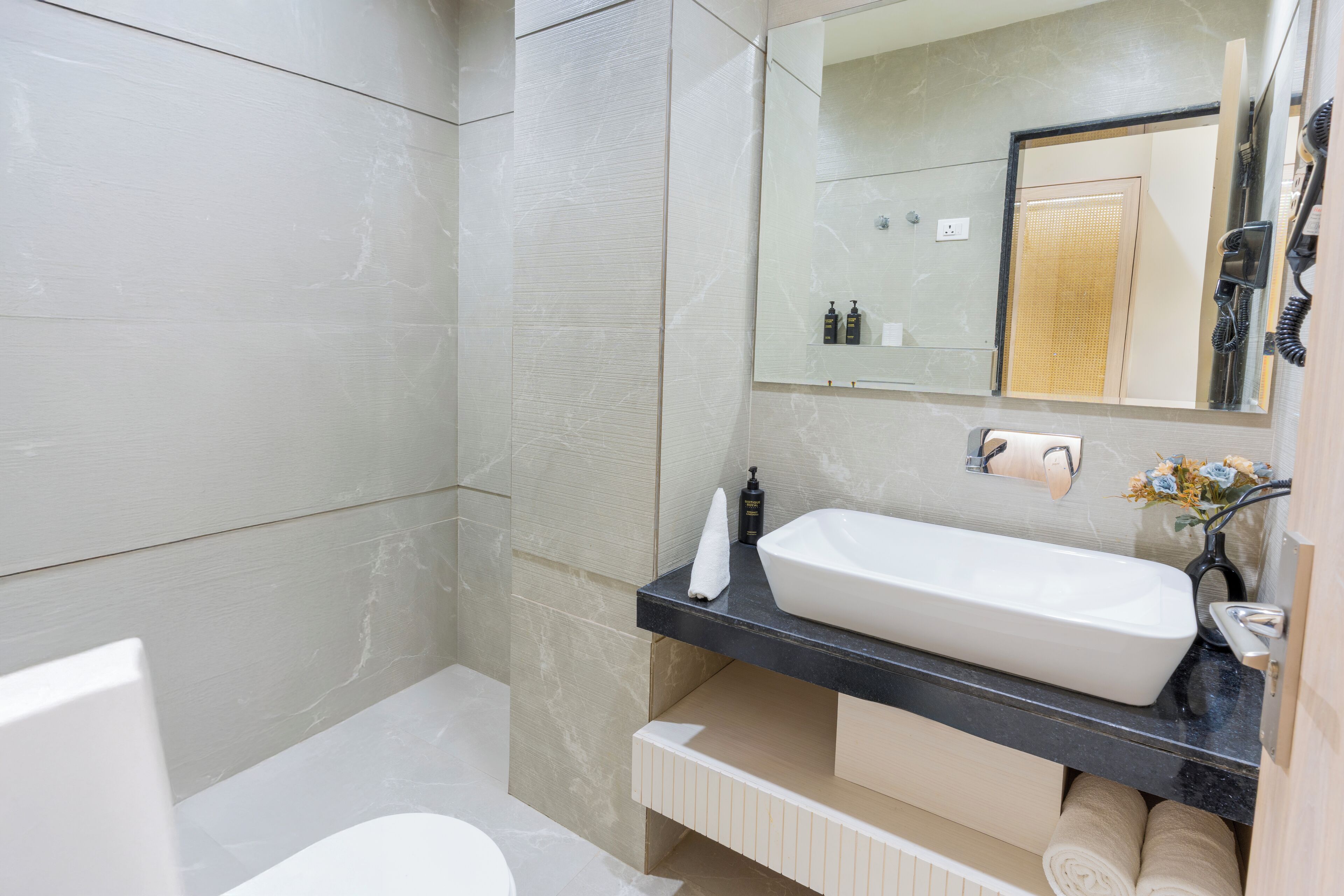 A modern bathroom with a white sink, black countertop, and beige tiles.