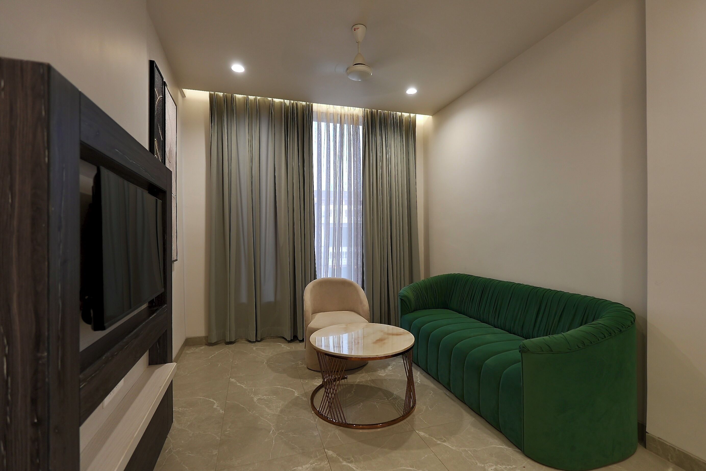 Una sala de estar con un sofá verde, una mesa redonda, un sillón color beige y un televisor sobre un mueble de madera oscura.