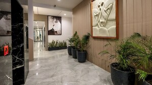 A modern hotel lobby with a marble floor, potted plants, and a large abstract wall art piece. - Elinor Hotel (Agra)