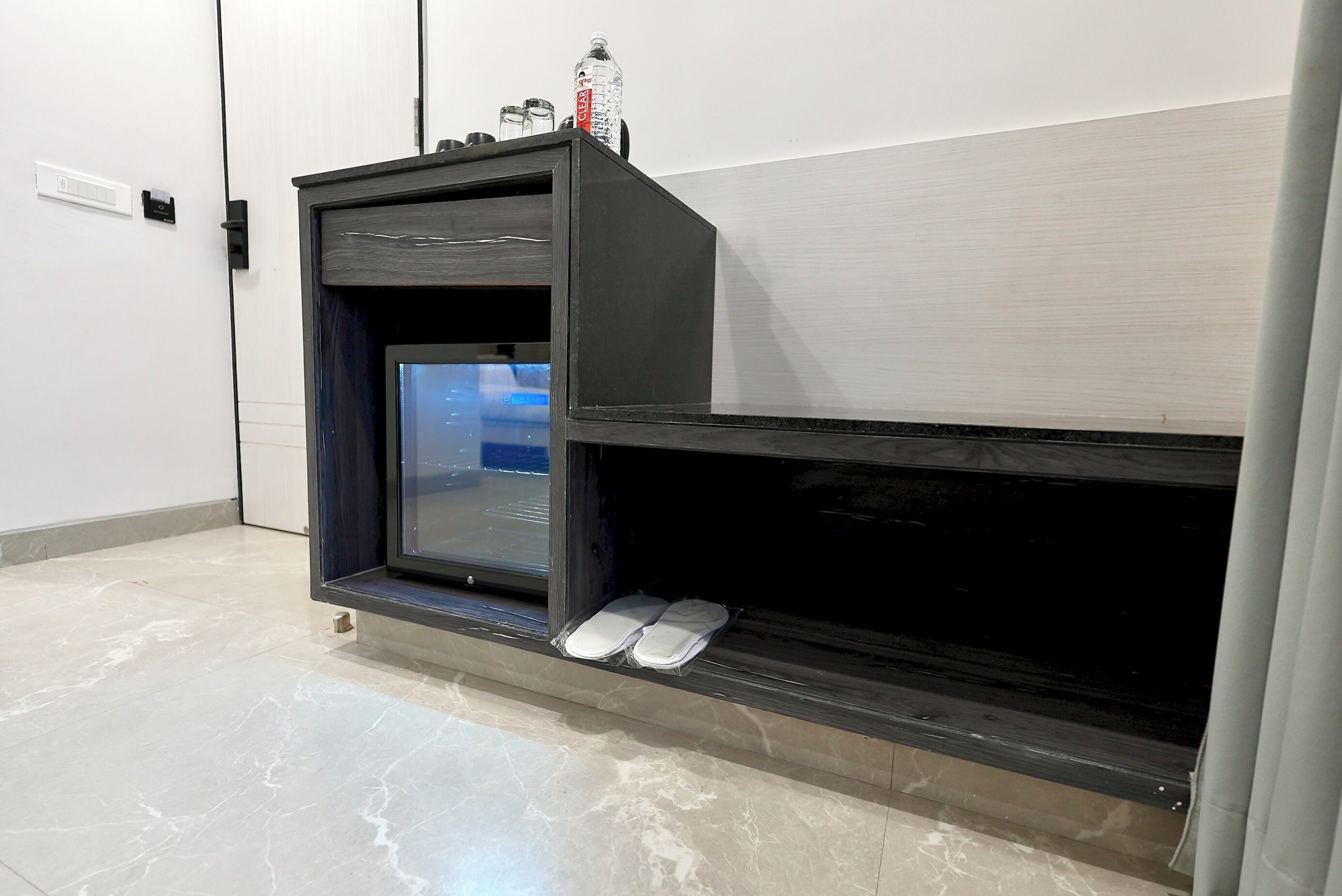 A modern room with a built-in TV, a shelf with shoes, and a bottle on top.