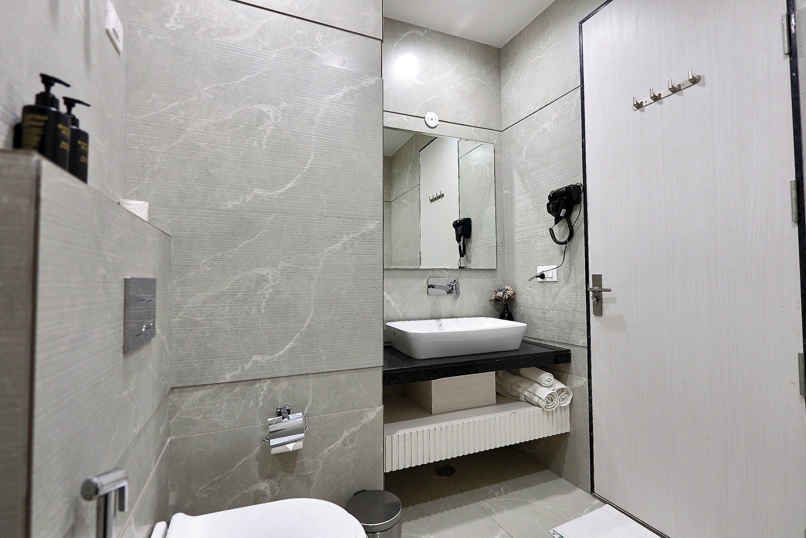 Un baño moderno con un espejo grande, un lavamanos blanco y un perchero para toallas.