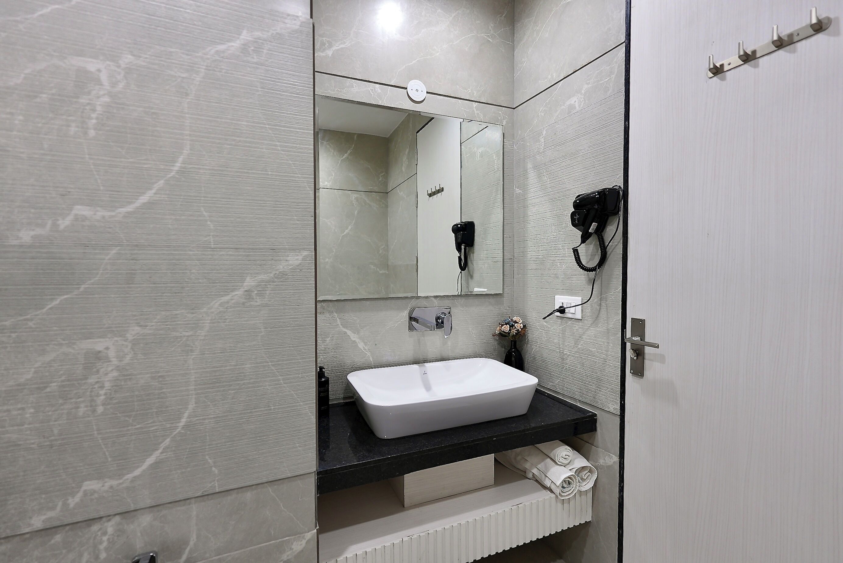 Une salle de bain moderne avec un lavabo blanc, un miroir et un sèche-cheveux fixé au mur.