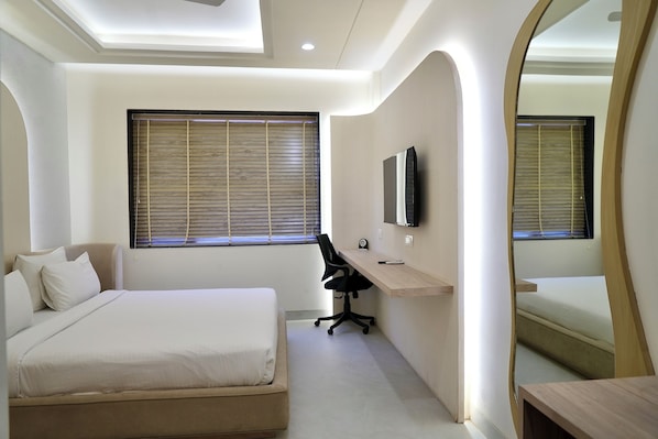 A bedroom with a bed, a desk, a chair, a TV, and a large mirror. - Elinor Hotel (Agra)
